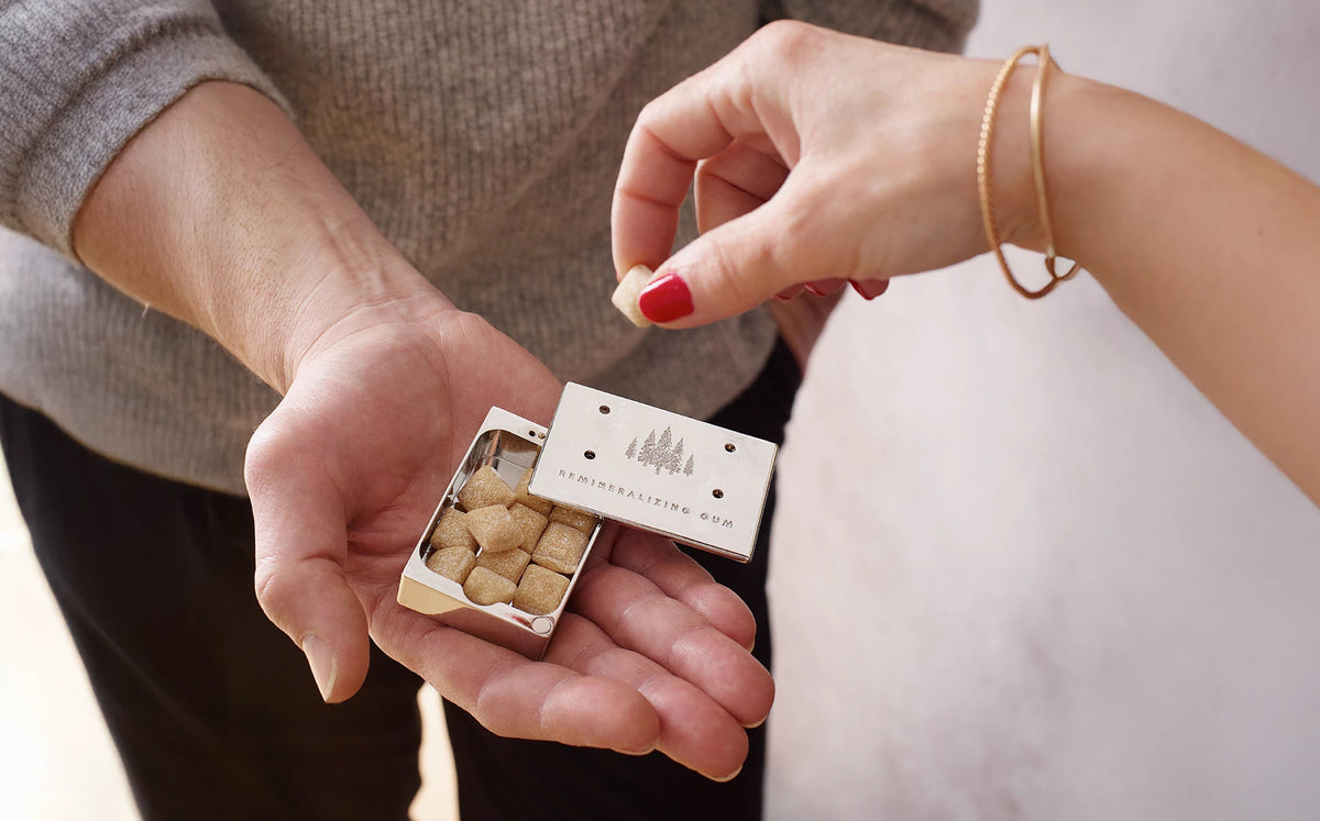 Hand taking eknest gum cube from Stainless Slide Snap Gum Case that is offered by another hand
